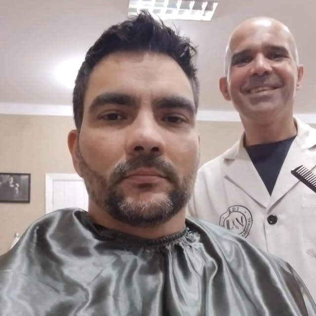 Cliente de barba cheia na cadeira, com o Edi ao fundo